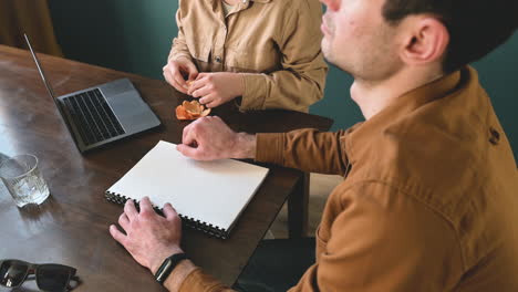 Blind-Man-Reading-A-Braille-Book-And-A-Woman-Peeling-A-Tangerine-While-Sitting-At-Table-At-Home