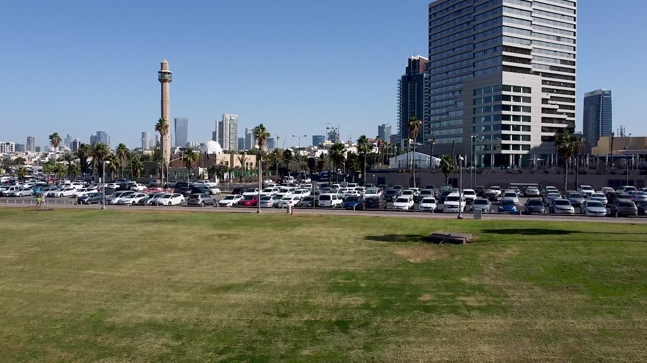 텔아비브의 한 공원 가장자리에 있는 자동차로 가득 찬 주차장의 공중 상승 전방 드론 샷