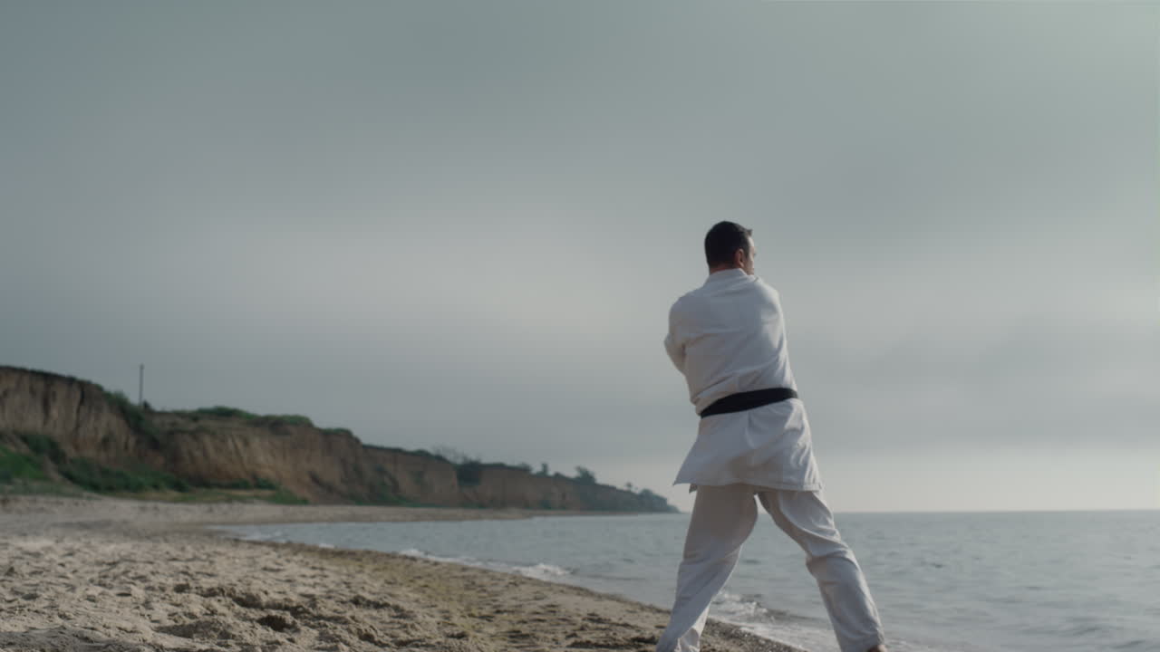 atleta de karate practicando patadas en una playa soleada. hombre deportivo entrenando artes marciales
