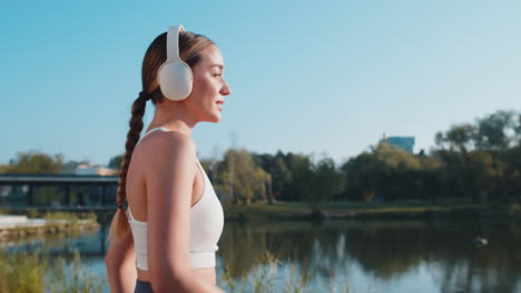 athletic fitness sport runner girl training putting on wireless headphones and jogging in park