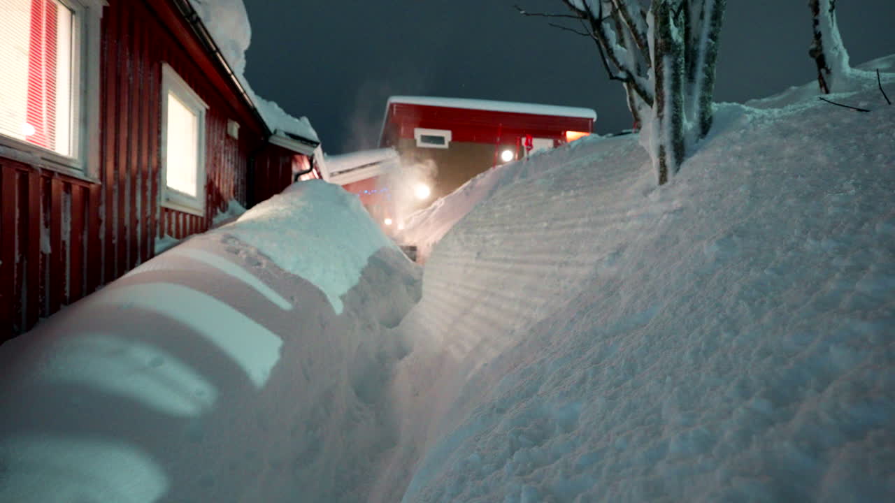 A snowplow clearing thick snow outside buildings in Tromsø, Norway, winter urban landscape, man pushing equipment in narrow pathway