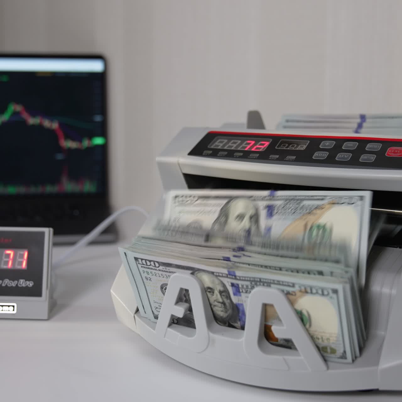 Un uomo inserisce un pacchetto di banconote da cento dollari in una macchina conta soldi. Banconote statunitensi contate con un dispositivo. Laptop con grafico sullo sfondo sfocato