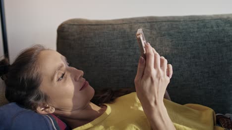 Caucasian woman lying on sofa and browsing phone
