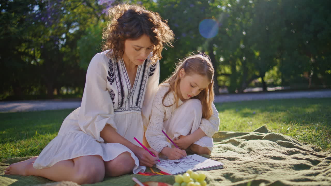 Woman child drawing picnic at sunny meadow together. Family weekend at nature