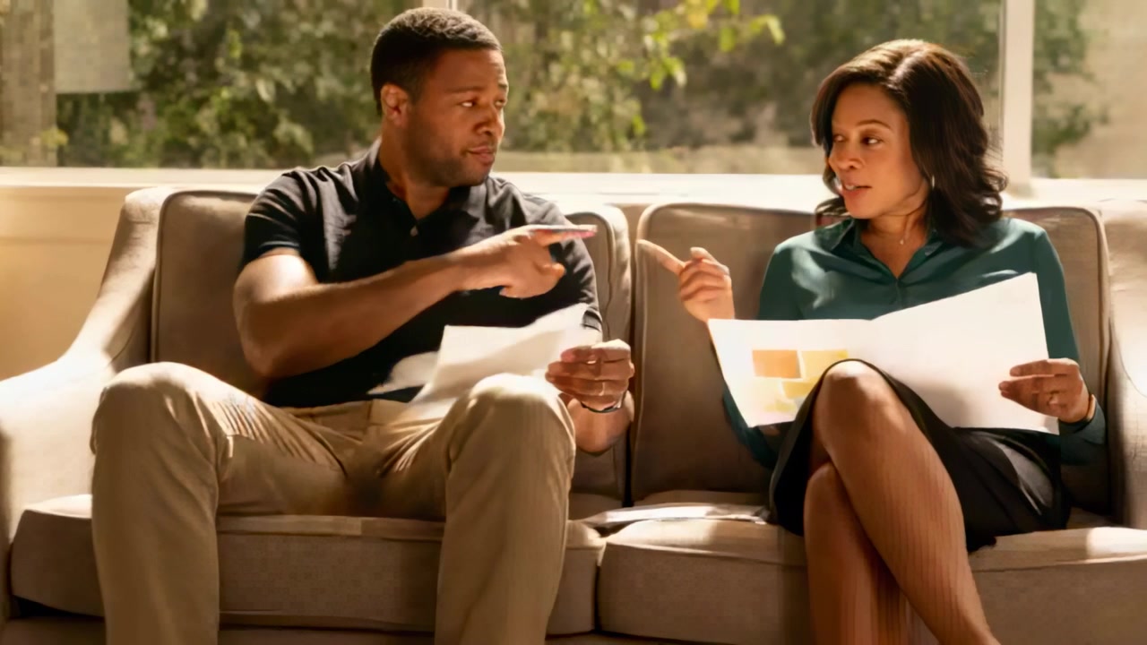 Glancing at swatches couple in black polo, teal blouse pointing, pen-marking choices on beige sofa