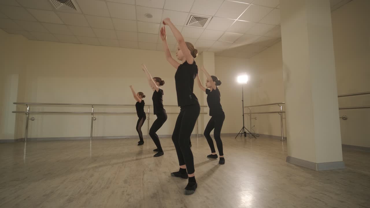 un grupo de jóvenes estudiantes de ballet con ropa de baile negra practicando posiciones en un amplio estudio de ballet con pisos de madera y barras montadas en la pared. expresiones enfocadas y movimientos sincronizados.