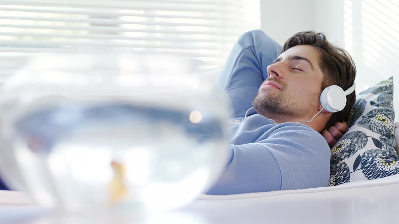 금색 물고기 그 ⁇ 과 소파에 누워 있는 남자가 헤드폰을 착용하여 음악 4k 4k를 나열하고 있습니다.