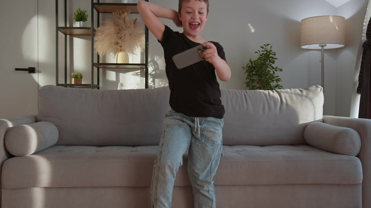 Young boy engrossed in playing games on a tablet device while standing in a sunlit living room with