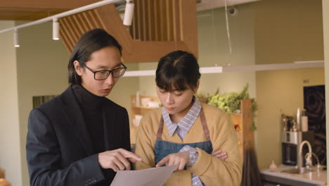 small business owner holding a paper and discussing about something with his female partner in coffee shop