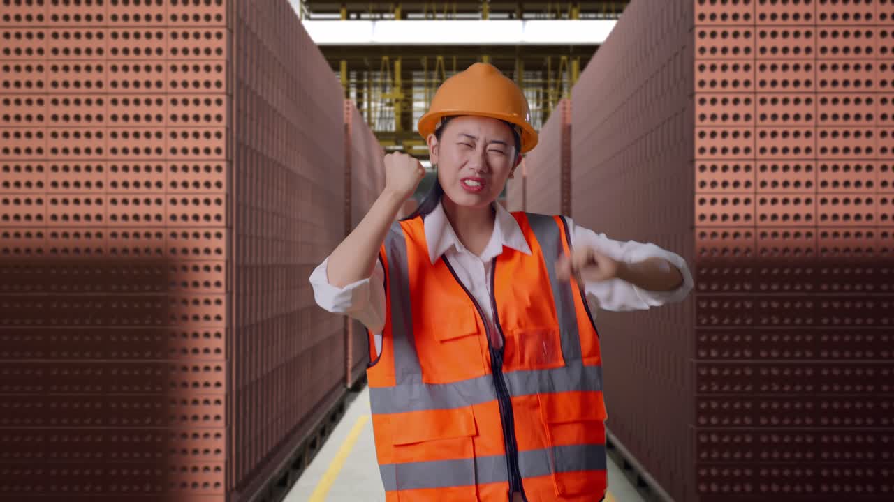 Asian Female Engineer With Safety Helmet Screaming Goal And Dancing Celebrating With Red Brick Packed in Stacks Are Stored