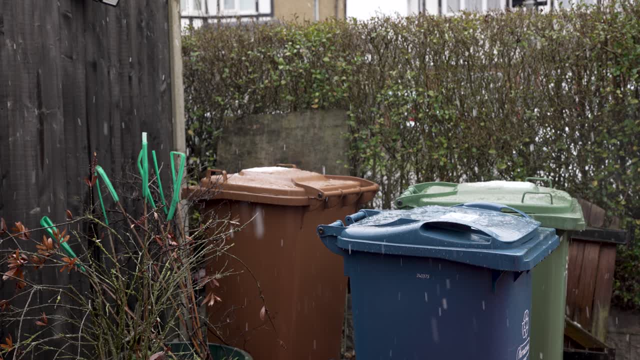 울타리 옆 정원 앞 정원의 쓰레기와 재활용 쓰레기통에 내리는 가벼운 눈