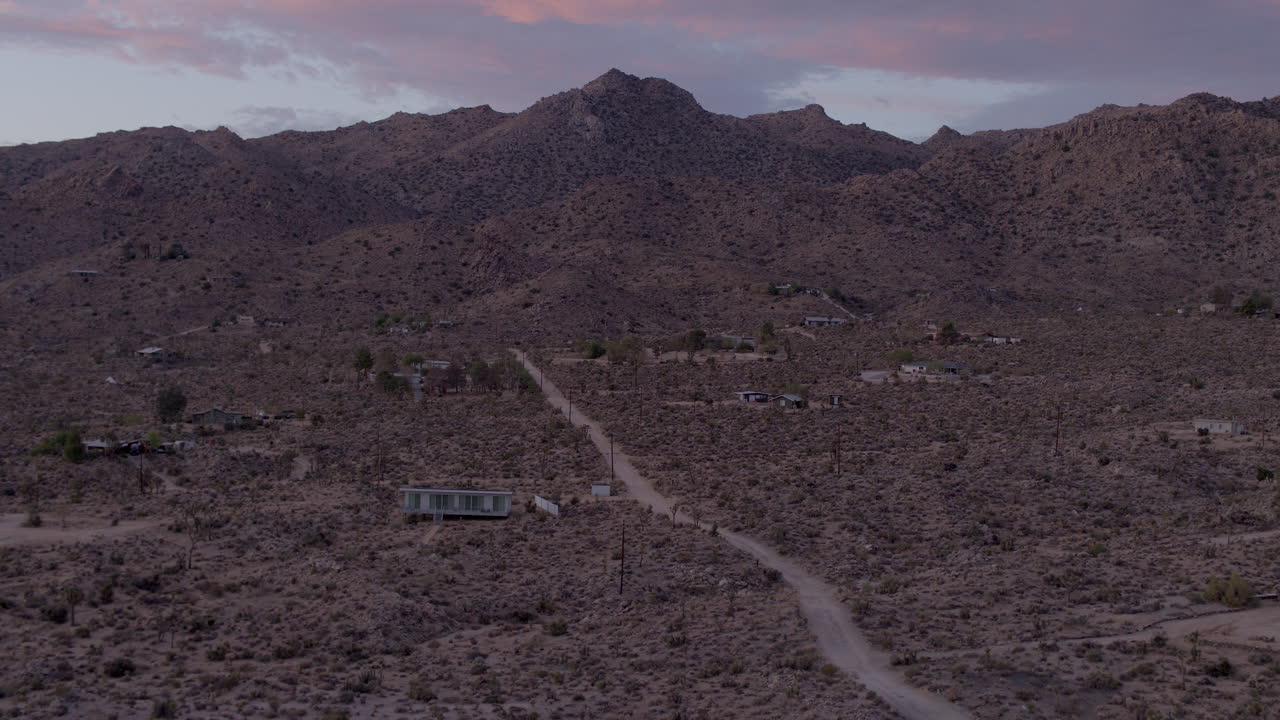 casas de sobrevuelo y camino de tierra hacia las colinas del parque nacional joshua tree en california al atardecer en una hermosa tarde