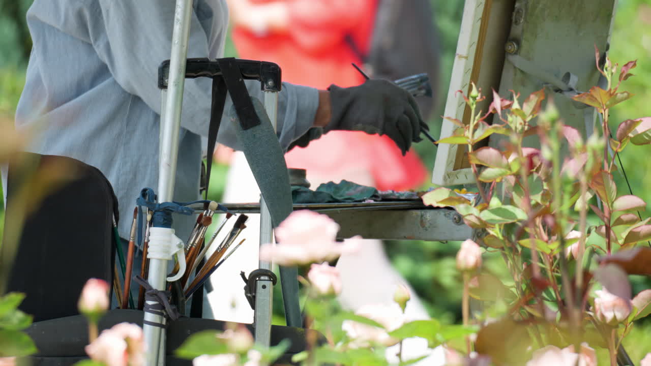 Mature Woman Oil Painting Roses in a Park Standing By Canvas on Easel and Picking Paint Colors From Palette