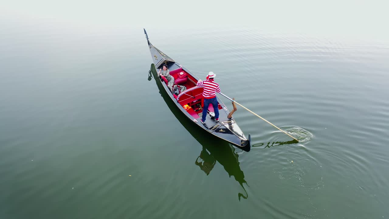 Beautiful woman sailing in gondola. Gondolier with oar moving boat slowly. Gondola floating the calm river in the evening.