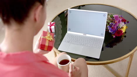 biracial teenage girl holding gift having laptop video call with copy space screen, slow motion