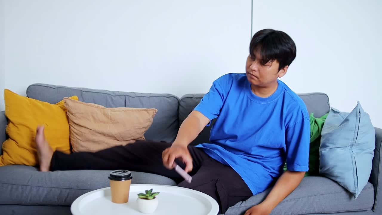 Young man relaxing on sofa scrolling smartphone casual comfort modern lifestyle leisure time