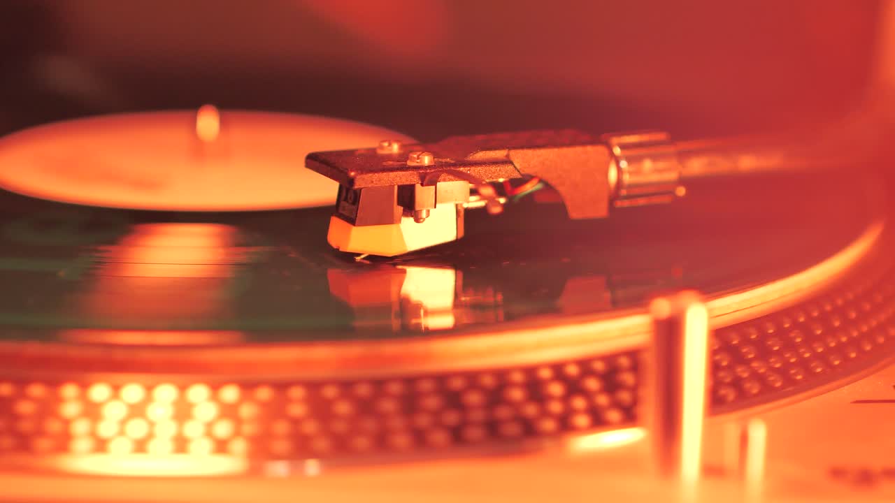 A Rotating Vinyl Record on a Turntable in the Light of a Warm Orange-Red Lamp. A dusty green colour LP Vinyl Disc Record Close-up Playing Music. Type A.