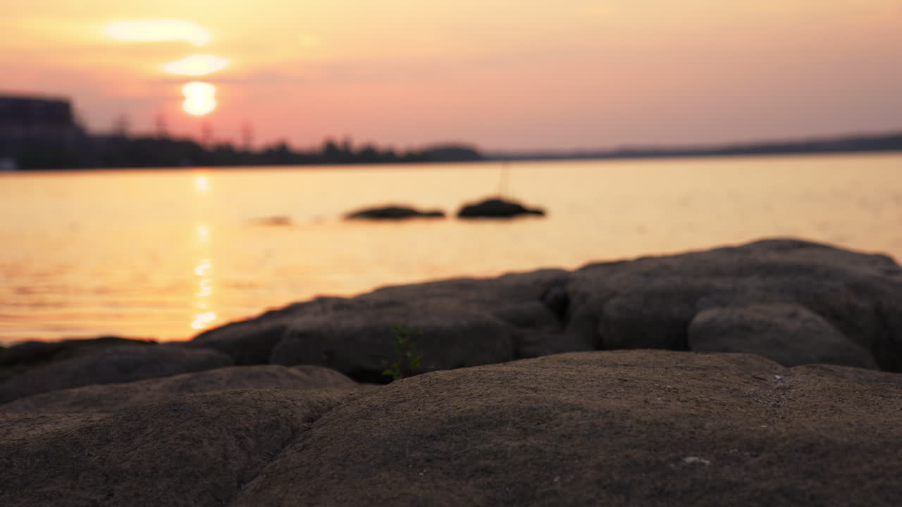 Rocky shore of the river at setting sun. Beautiful colors of sundown near water. Dark silhouettes of the nature at the other side of the river. Blurred backdrop.