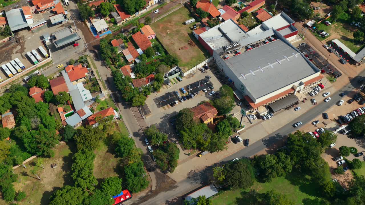 Drone video capturing a sunny aerial view of a bus depot nestled in lush greenery in Areguá, Paraguay. Bright daylight enhances the scenic contrast between vehicles and nature