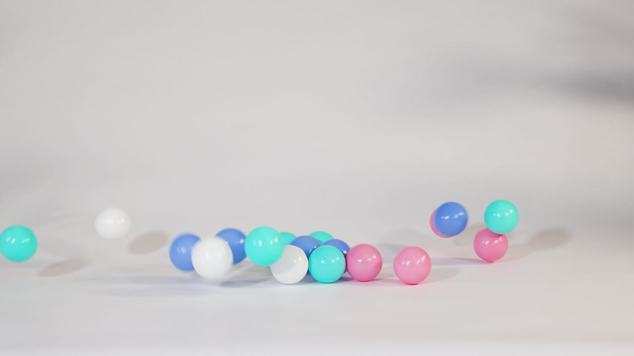 Bola-bola plastik berwarna merah muda cerah, biru, dan turquoise jatuh dan memantul dengan latar belakang putih bersih