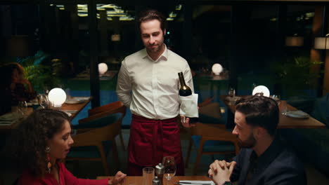 restaurant waiter pouring wine serving beautiful couple at fancy cafe table.