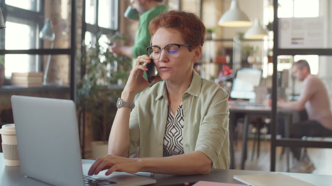 Woman working on laptop and talking on the phone in an office