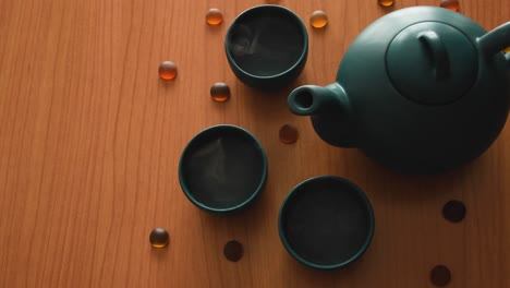 minimal background of a green japanese tea set with steam coming out of the cups, on a wooden table, with some stones around