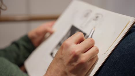 close up of artist's hands drawing a face on sketch pad with pencil while seated