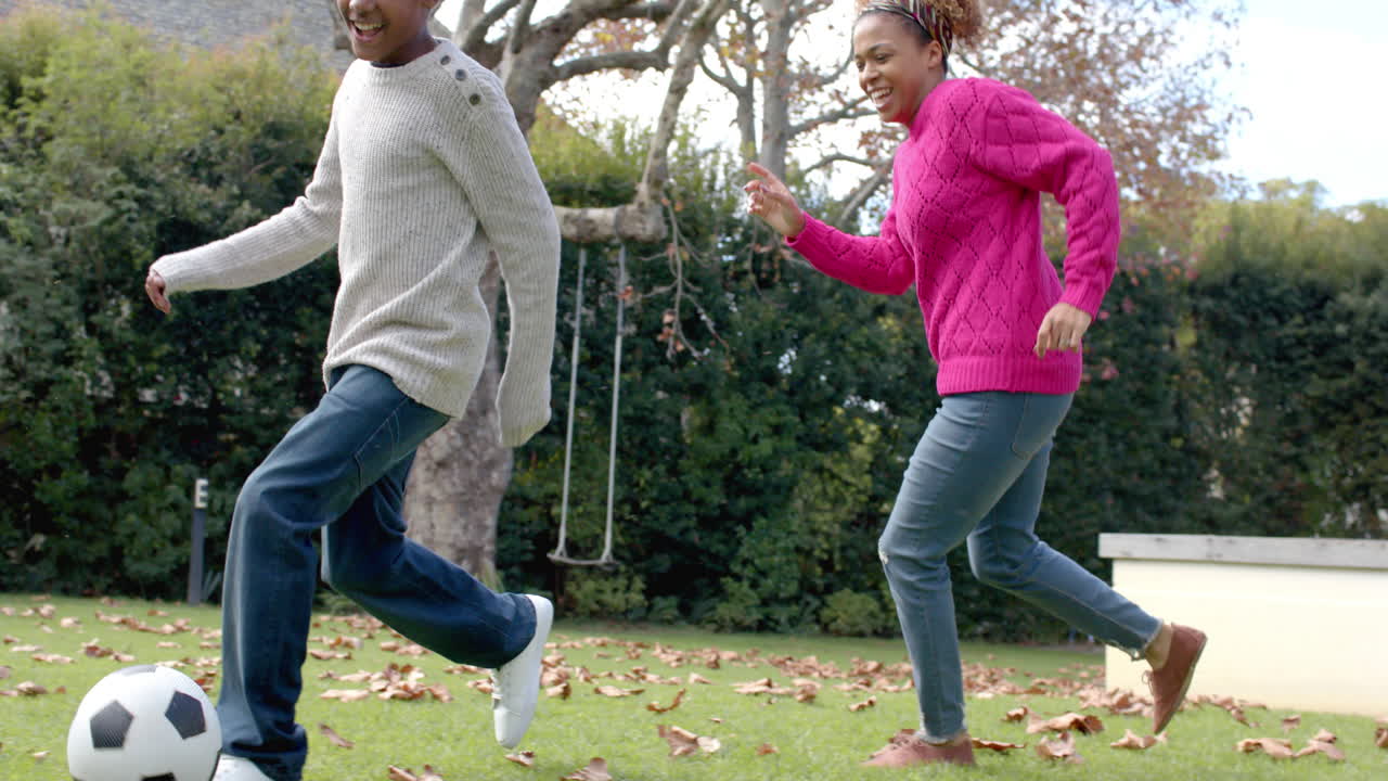 Happy african american mother and son playing football in garden, slow motion