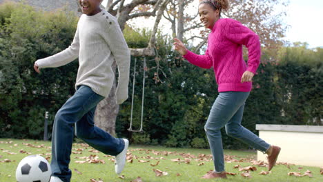 happy african american mother and son playing football in garden, slow motion