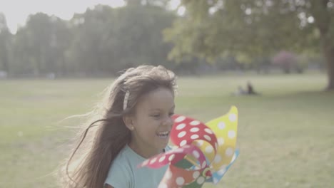 chica latina sosteniendo abanico de papel, corriendo y sonriendo en el parque