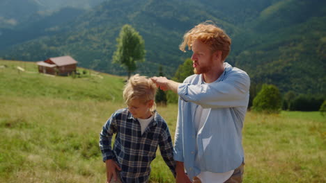 Man-son-enjoy-mountains-walk-closeup.-Smiling-father-ruffling-boy-hair-on-hill.