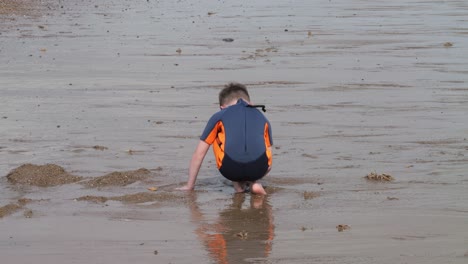 Young-boy-in-a-wetsuit-on-a-beach-digging-in-the-sand