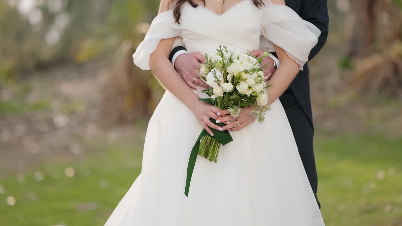 Brudeparret omfavner hinanden, mens de holder en hvid blomsterbuket i bryllupstøj.