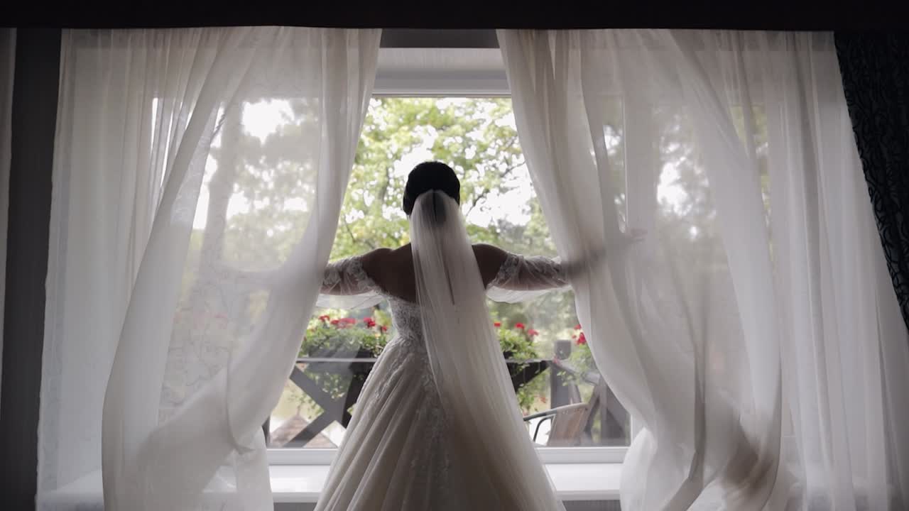 hermosa novia en vestido de novia blanco de pie en una ventana