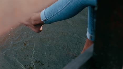 Cerrar-Las-Piernas-De-Una-Mujer-Colgando-Sobre-El-Agua-Una-Joven-Disfrutando-Del-Tiempo-Sola-Sentada-En-Un-Puente-De-Madera-En-El-Parque