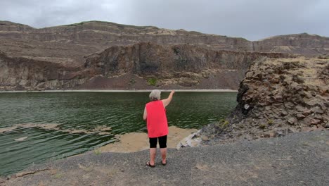 senior, female pointing to the cliffs surrounding alkali lake in northern washington state on a cloudy, breezy afternoon