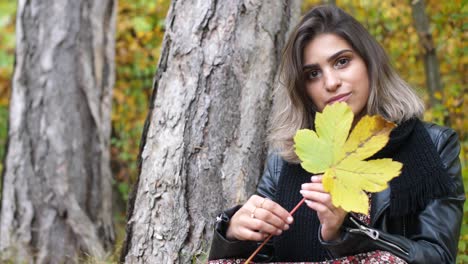 brunette girl in the autumn forest holds a yellow leaf in her hand and spins it near her face