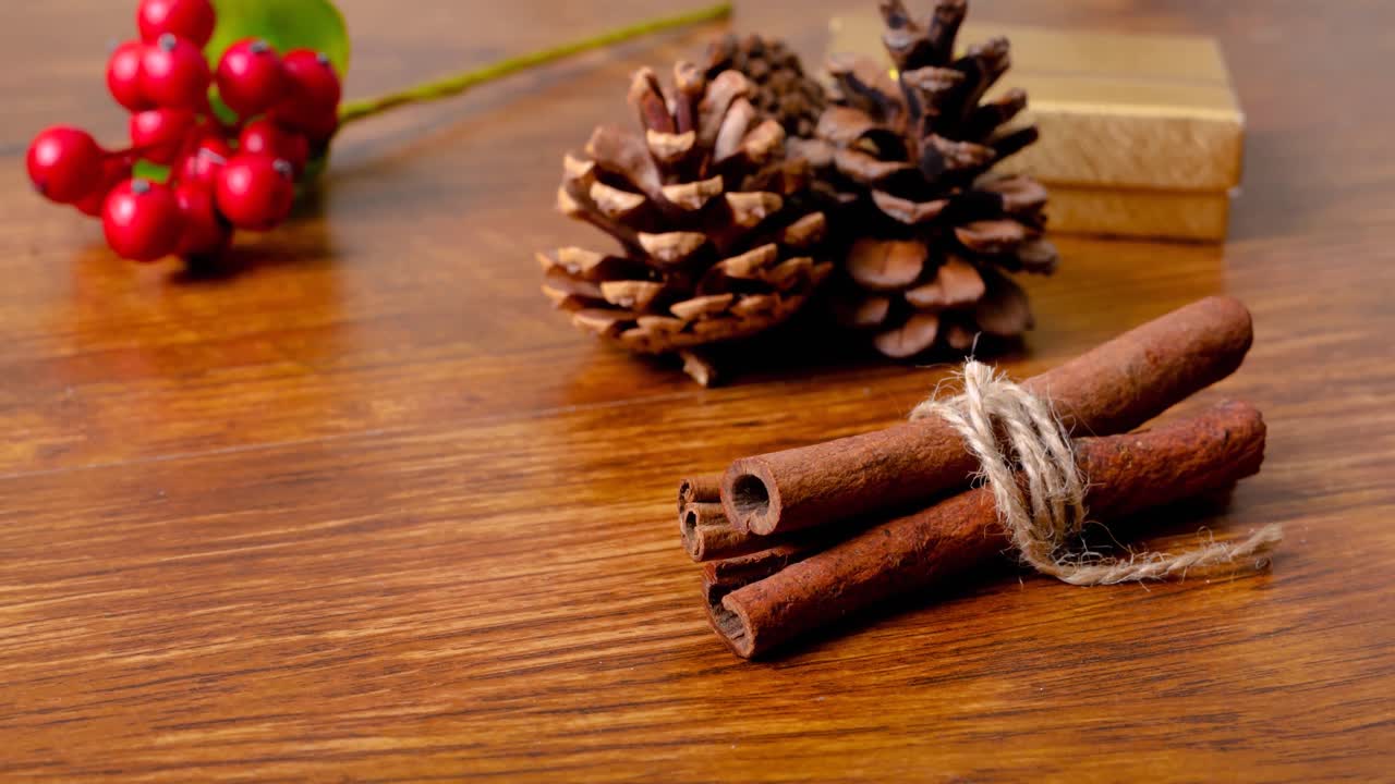 Animação de decorações de Natal, canela, pinhas e espaço para texto em fundo de madeira.