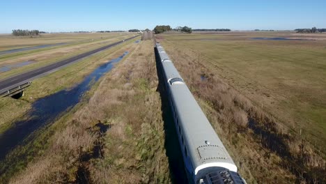 passenger train on the outskirts of buenos aires, moving through a rural landscape, clear blue sky above, daylight