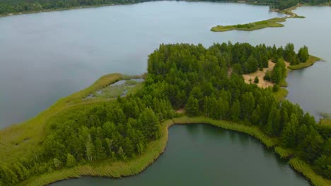 aerial orbit around small island and peninsula in middle of the artificial lagoon from past sand mining at männiku lake former quarry. green trees on the islet sway in the wind during moody summer day