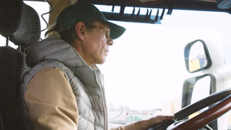 close up view of older worker wearing cap and vest driving a truck in a logistics park