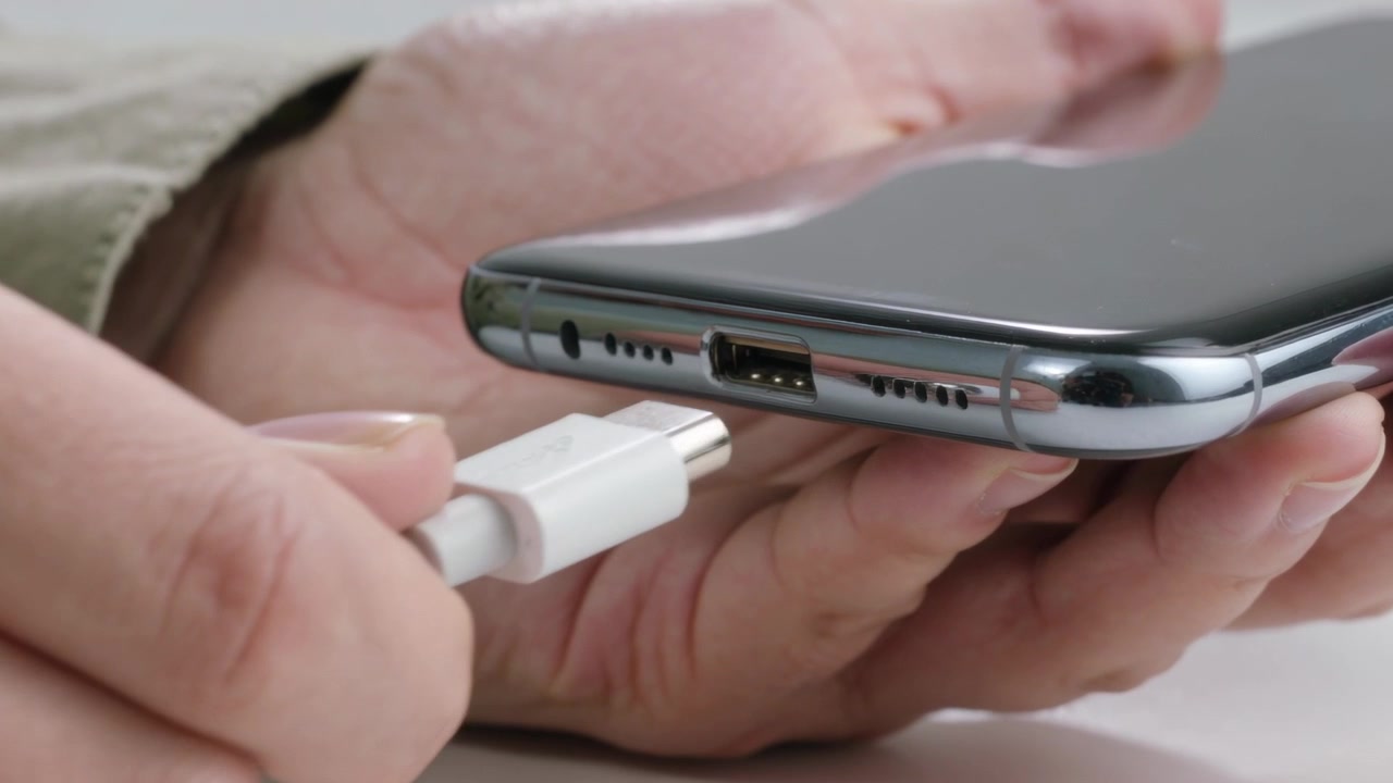 Tenendo il telefono nel palmo, le mani si allineano, inserendo un cavo bianco nella porta su un tavolo bianco per caricarlo.