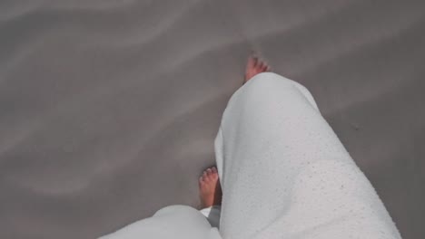 a person in white sweat pants walking barefoot over a white sandy beach