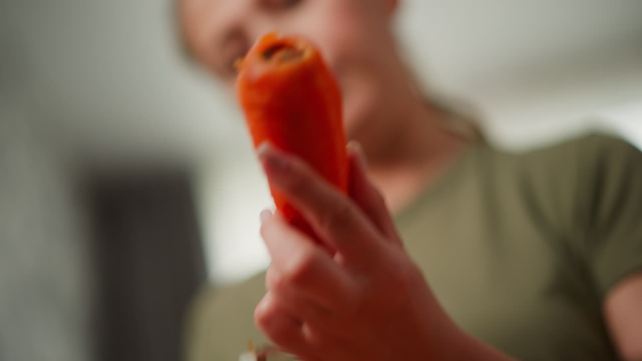 Close up of woman using peeler tool to skillfully peel carrot skin under soft blur background focus on hand movement and skin removal with peel curling during fresh vegetable prep