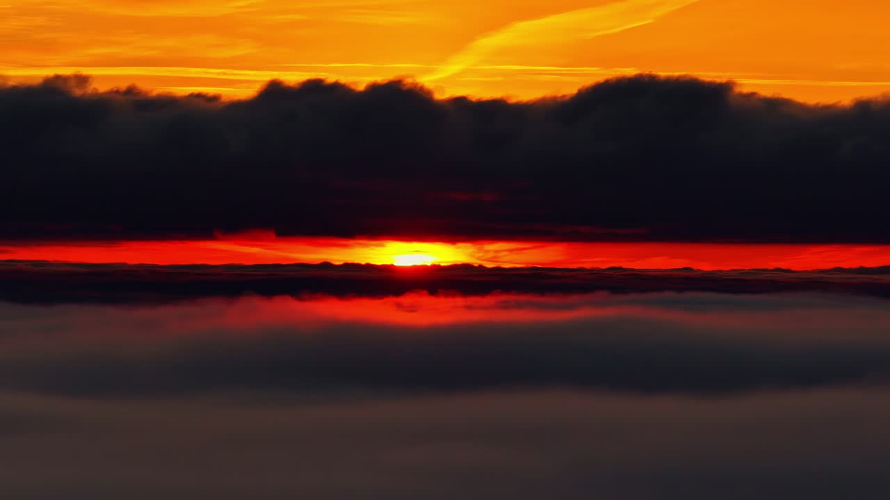 Dramatisk solopgang over et skylag, hvor dybt orange lys skinner under en mørk skypakke, hvilket skaber en skarp horisont af farve og kontrast