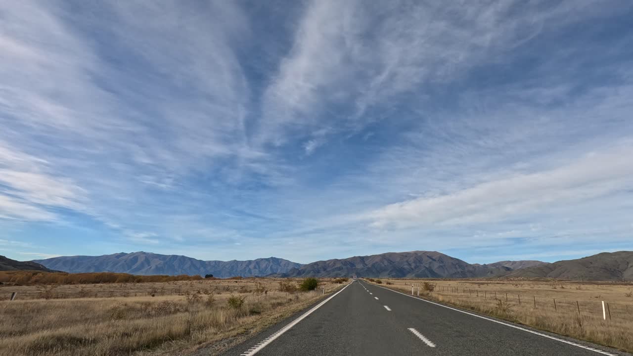 A serene drive along a highway with expansive skies and distant mountains in Lake Tekapo, New Zealand, during autumn