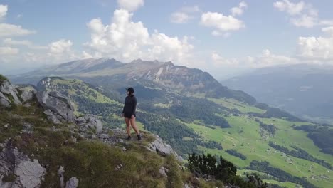 Orbitando-Alrededor-De-Una-Chica-Asiática-Con-Un-Sombrero-Que-Se-Encuentra-En-La-Cima-De-Una-Montaña-Y-Disfruta-De-La-Hermosa-Vista-Del-Lago-Walen