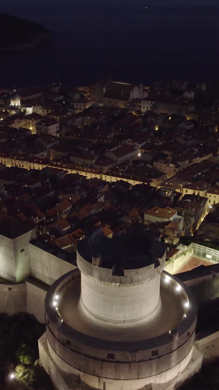 Aerial view of the illuminated Minceta Tower and Dubrovnik Old Town at night, Croatia. vertical video