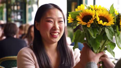 joyful interaction: a young woman delights in receiving a beautiful bouquet of sunflowers while enjoying a charming café experience with friends